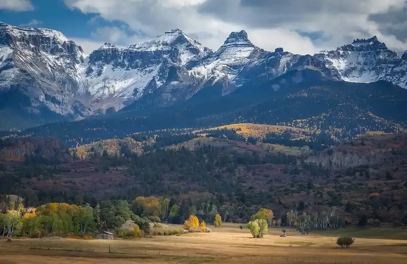 Log cabin on a ranch meadow beneath the snow-capped San Juan Mountains