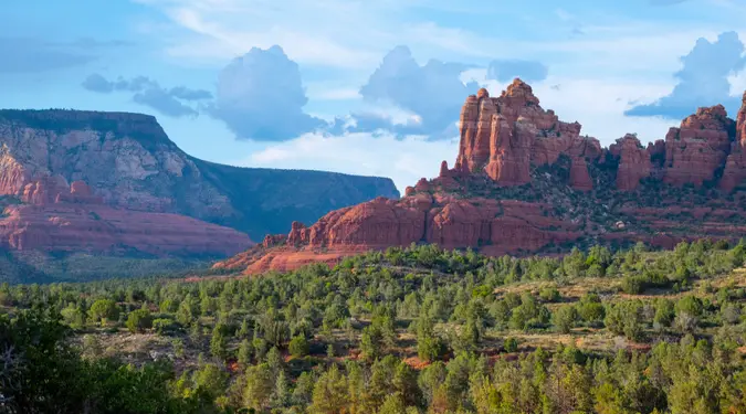 Sedona red rock formations above a green juniper valley in soft evening light