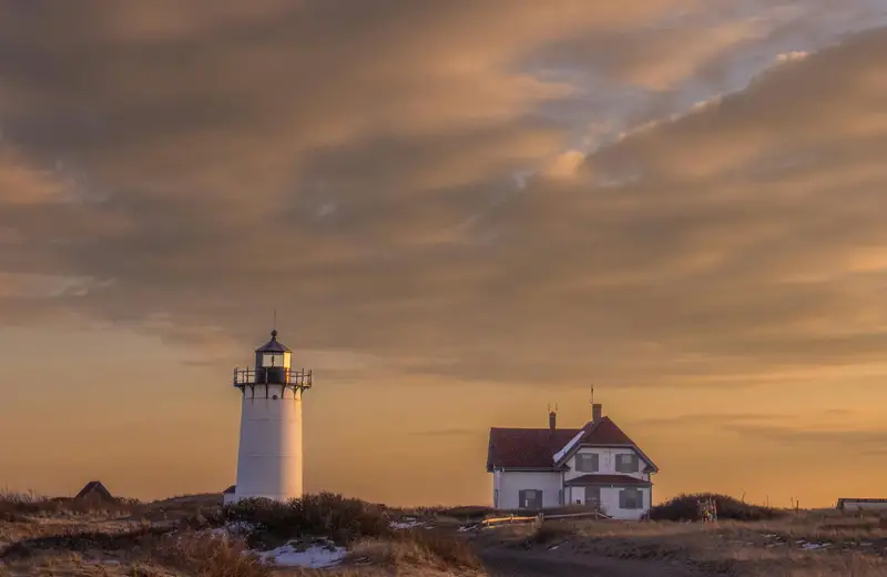 A Cape Cod lighthouse at sunset near beach hotels with in-room hot tubs