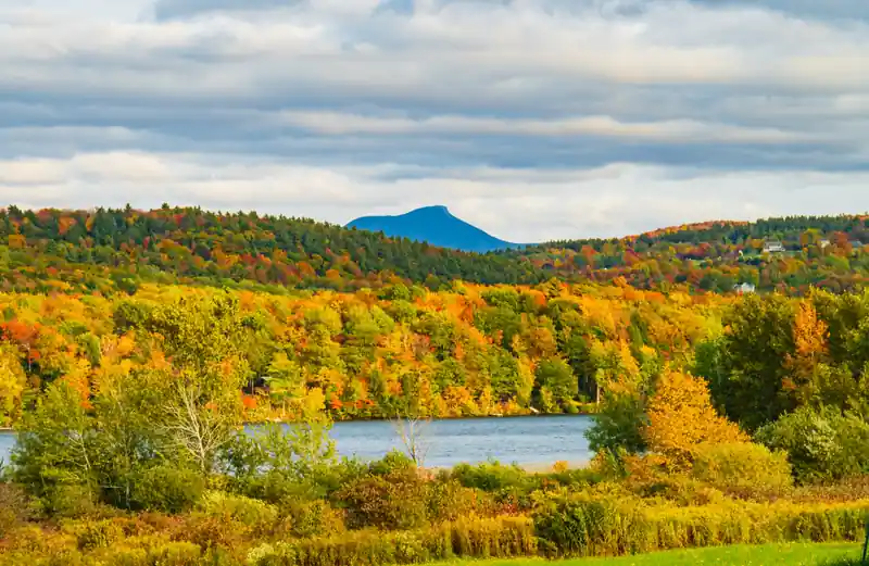 Camels Hump mountain above a Vermont lake surrounded by golden autumn trees