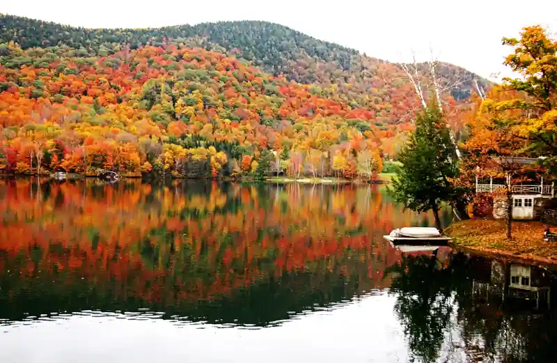 Vermont lake reflecting a blazing red and orange autumn hillside beside a boathouse